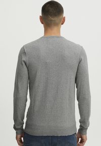 Grå strikkegenser med rund hals, lange ermer og ribbestrikket kant. Myk tekstur og vanlig passform. Uten mønstre eller pynt.