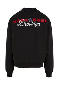 Hanorac negru cu broderie pe spate în text roșu, alb și albastru cu "KARL KANI" și "Brooklyn". Guler clasic și manșete ribbate.
