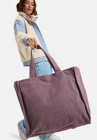 Fioletowa torba typu tote wykonana z korduroju, z dwiema rączkami, z subtelnym logo z przodu. Torba jest przestronna i ma wyraźny kształt.