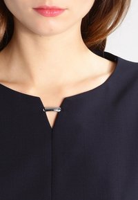 Robe bleu marine présentant un décolleté en V avec un accent métallique et une texture de tissu élégante. Vue rapprochée mettant en avant le design du col.