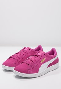 Baskets en daim rose avec accents blancs, bout rond, fermeture à lacets à l'avant, col rembourré et détail du logo doré sur le côté. Semelle en caoutchouc plate.