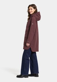 Lange, bordeauxrood waterdichte jas met een capuchon, drukknoopsluiting en zijzakken, gecombineerd met wijduitlopende blauwe jeans en zwarte laarzen.