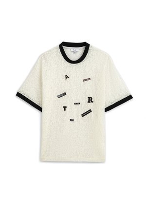 Haut court en dentelle blanche à manches courtes avec col et poignets noirs, orné de patchs noirs et blancs représentant des lettres et des mots éparpillés.