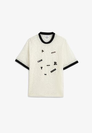 Top de encaje blanco de manga corta con cuello y puños negros, decorado con parches dispersos de letras y palabras en negro y blanco.