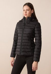Svart puffjacket med høy krage, glidelås foran og horisontale baffler. Den har sidelommer og en glatt, glinsende overflate.