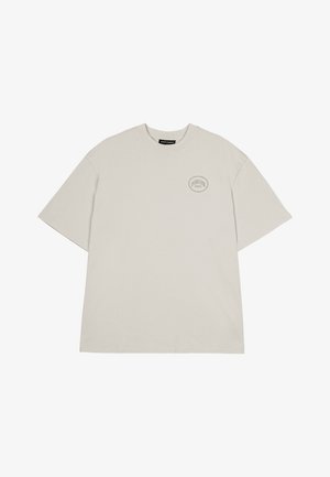 Helehallist puuvillane T-särk, millel on ümar kaelus, lühikesed varrukad ja väike ringikujuline logo vasakus rinnapiirkonnas. Lihtne, vabalt voolav lõige.