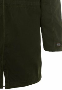 Chaqueta impermeable de manga larga en verde oscuro, con costuras visibles y un parche de marca redondo cerca del puño, sobre un fondo blanco.