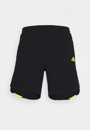 Czarne sportowe szorty z neonowo-żółtym logo Adidas na prawej nogawce oraz perforowanymi wzorami wentylacyjnymi blisko dolnej krawędzi.