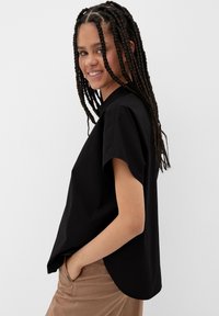 Zwarte korte mouw shirt met een losse pasvorm en ronde zoom, gemaakt van katoen. Gecombineerd met lichtbruine broek voor contrast.