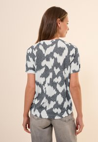 T-shirt en tricot à manches courtes de couleur bleu clair avec un motif abstrait noir. Présente une coupe décontractée et un col ras du cou, accentué par une finition texturée.