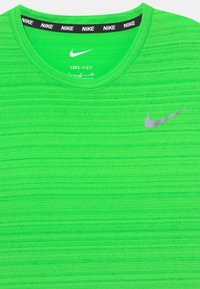 Camiseta verde Nike Dri-FIT con cuello redondo, patrón de rayas texturizadas, logo reflectante en plata en el pecho y banda de cuello interior negra.