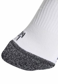 Λευκή αθλητική κάλτσα με γκρι πλεκτή φτέρνα και μύτη. Διαθέτει ριγωτή υφή στο πάνω μέρος και μαύρο λογότυπο κοντά στον πάτο.