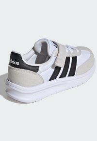 Chaussure de sport blanche avec des accents en suède gris et des rayures noires. Dotée d'une sangle à velcro et d'une semelle en caoutchouc texturé pour une meilleure adhérence.