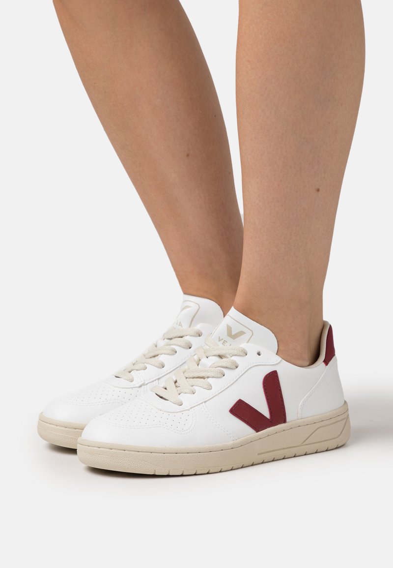 Sneakers bianchi in pelle traforata, suola in gomma beige, logo bordeaux di lato e lacci beige, progettati con una silhouette a bassa forma.