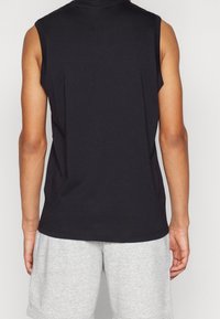 Svart ärmlös skjorta i mjukt bomullstyg. Har en enkel, ren design med sidopp slit, ihop parat med ljusgrå shorts.