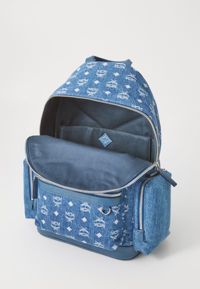 Zila denim mugursoma ar rakstainu audumu un ādas akcentiem; ietver lielu galveno nodalījumu, priekšējo kabatu un sānu rāvējslēdzēju.