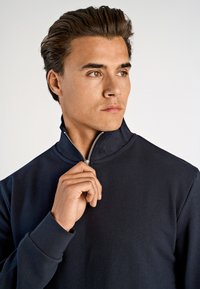 Sudadera azul marino con cuello alto y cremallera en el cuello, que cuenta con una cremallera plateada y puños acanalados. El material parece suave y elástico.