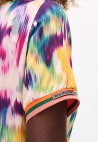 Camicetta a maniche corte realizzata in tessuto colorato e liscio, caratterizzata da un vivace motivo tie-dye. Rifinita con strisce multicolori nei polsini.