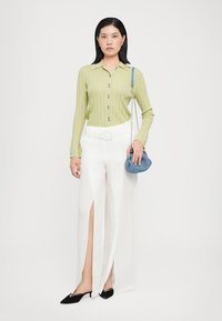 Light green ribbed knit shirt with buttons, white wide-leg trousers with slits, black pointed flats, and a small blue textured handbag.