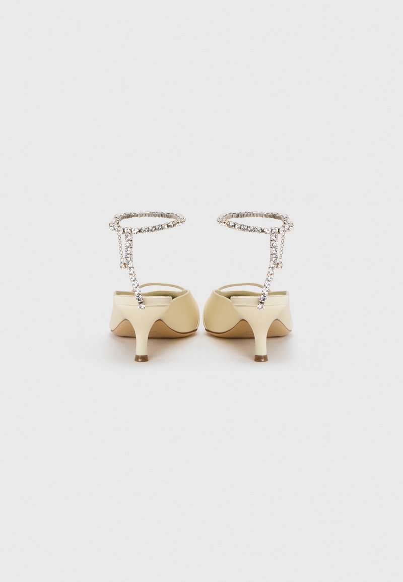 Beige kitten heel sandaler med rhinestones ankelsnor, set fra ryggen på en simpel hvid baggrund.
