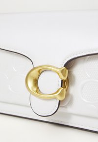 Witte leren handtas met een getextureerd paneel, voorzien van een gouden metalen sluiting en contrasterende randen. Gladde afwerking met een subtiel logo-patroon.
