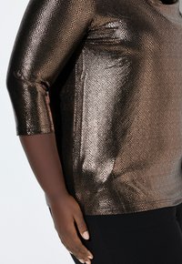 Metallisk bronze topp med ett orm mönster, 3/4 ärmar och en slät yta. Matchad med svarta byxor som har en figurnära design.