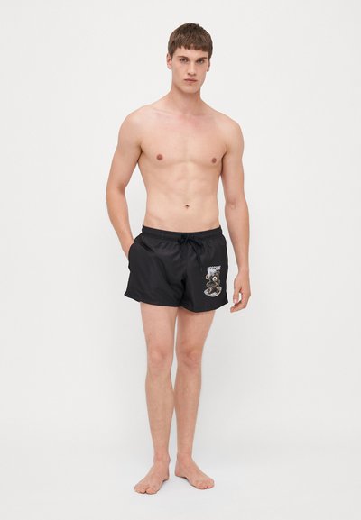 Shorts de bain noirs en matériau léger, avec un design brodé sur le côté gauche, une taille avec cordon de serrage et une coupe ample.