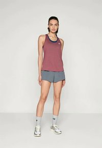 Αθλητική ένδυση που περιλαμβάνει ένα μπορντό αμάνικο μπλουζάκι με μπλε λεπτομέρειες και γκρι σορτσάκι. Το μοντέλο φοράει γκρι και λευκά αθλητικά παπούτσια με ανοιχτό γκρι κάλτσες.