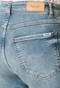 Světle modré džíny z denimu s texturovaným povrchem. Mají hnědou koženou nášivku na zadní části pasu a malou bílou nášivku na kapse.