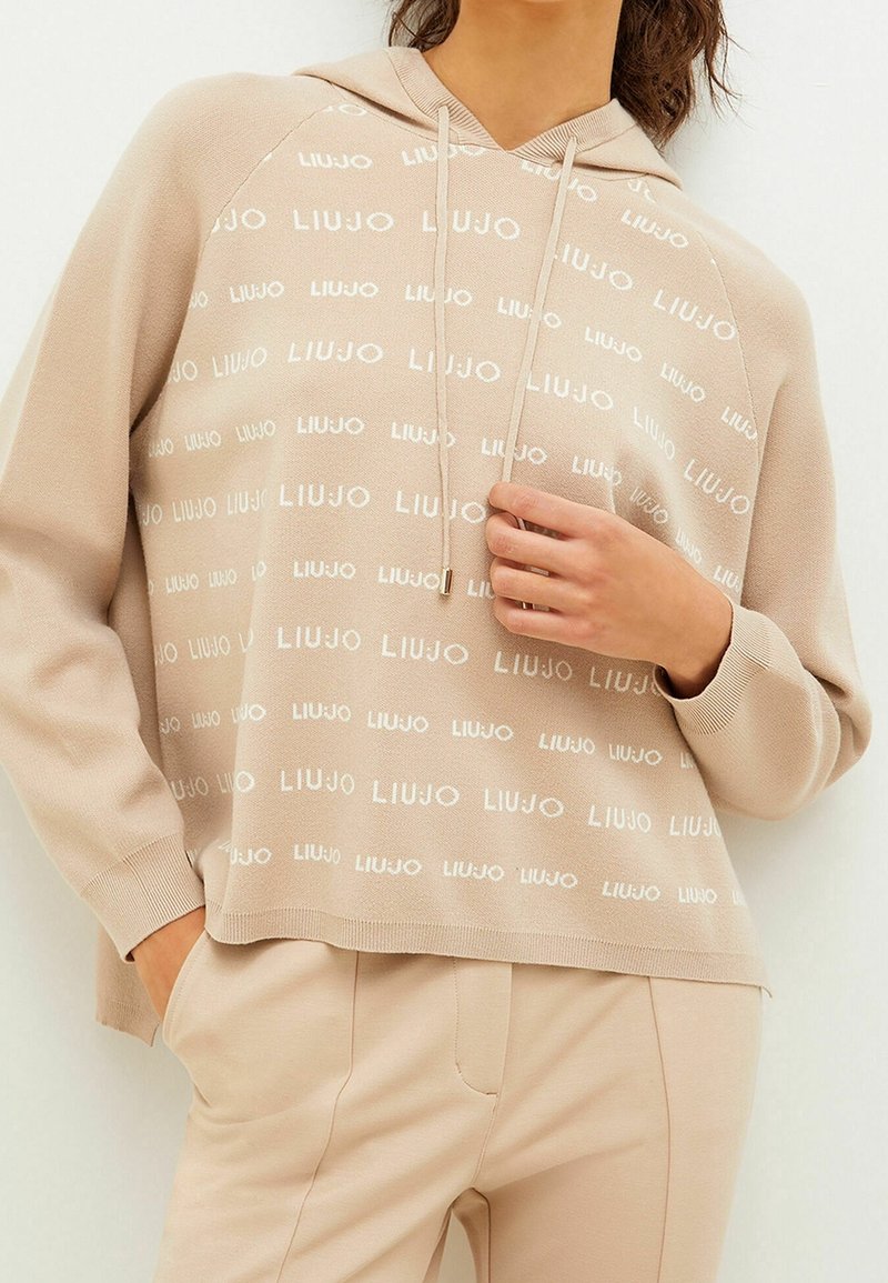 Beige hoodie met wit 'LIU JO' logo patroon, capuchon met trekkoord, geribbelde boorden en zoom. Gecombineerd met beige broek voor een coördinerende uitstraling.