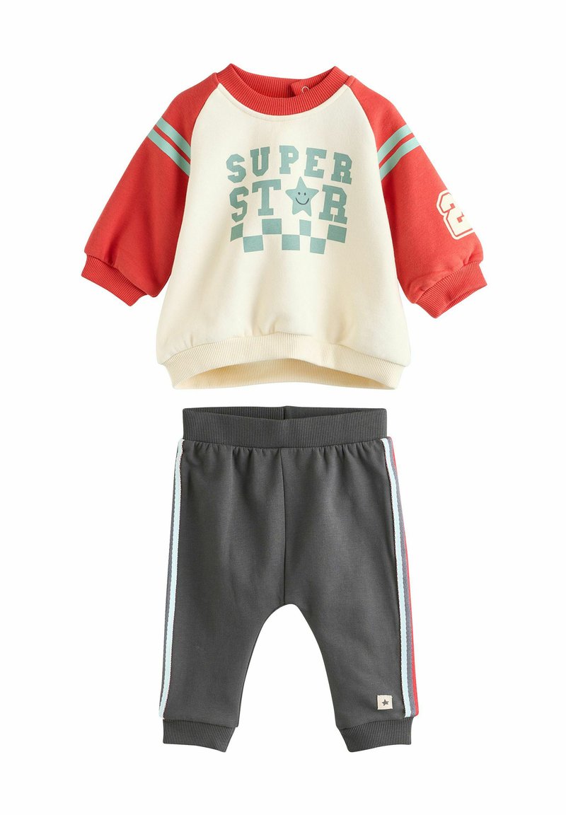 Sweatshirt i creme og rød med teal-striber og "SUPER STAR" grafik; parret med grå sweatpants med sidelister og afsluttede ankler.
