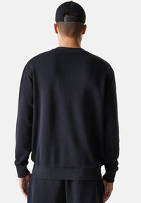 Felpa nera con collo rotondo, polsini e orlo a coste. Realizzata in tessuto morbido, progettata con una vestibilità ampia. Semplice, senza motivi visibili.