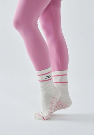 Białe skarpety z różowymi serduszkami i dwoma różowymi paskami, napis „Zostaw mnie w spokoju”, noszone z różowymi legginsami na jednolitym tle.