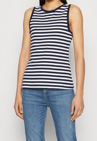 Marinblå och vit randig ärmlös topp i bomull, med rundad halsringning och figursydd passform, kombinerad med ljusblå jeans.