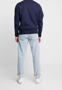 Felpa blu navy con polsini e orlo a coste, abbinata a jeans azzurri arrotolati e sneakers bianche. Tessuto liscio, vestibilità casual.