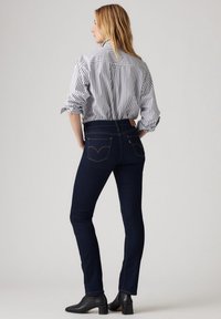 Jeans ajustados de mezclilla en un tono azul oscuro, con una cintura alta y bolsillos traseros con un logo bordado. Combinados con una blusa a rayas.