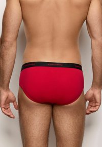 Rote Unterwäsche aus einem glatten Stoff, mit einem schwarzen Bund, der das 'yamamay'-Logo trägt. Entworfen mit einer figurbetonten Silhouette.