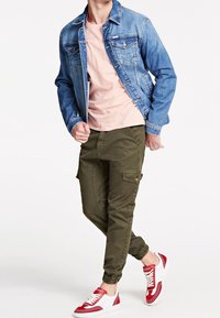 Farkkutakki, vaaleanpunainen t-paita, oliivinvihreät cargo-housut joustavilla lahkeilla ja punaiset sekä valkoiset tennarit. Ominaisuuksiin kuuluvat taskut ja ompeluyksityiskohdat.