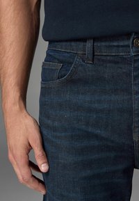 Tumedad sinised teksad tekstuurse denimkangaga. Omadusteks on eesmine tasku, õmblustooted ja nööbi sulgemine koos vöö kohta.