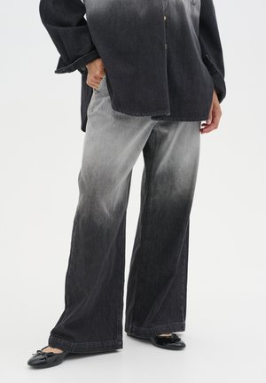 Black and gray denim wide-leg pants feature a gradient fade, with a relaxed fit and visible stitching. Worn with black ballet flats.