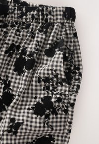 Tissu à motifs en noir et blanc présentant un motif à carreaux avec des accents floraux, légèrement froncé en haut, mettant en valeur la texture.