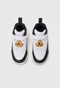 Tenisi albi și negri cu un design din piele și plasă, având un logo Jumpman auriu pe un patch triunghiular și o curea Velcro.