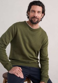 Mörkgrön stickad tröja med rund halsringning och ribbade muddar, med mjuk textur och avslappnad passform. Bärs över en vit skjorta.