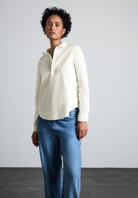 Cremefarvet skjorte med lange ærmer og uden knaplukning, parret med lyseblå vide jeans. Glat tekstur, afslappet pasform.