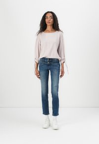 Lys rosa ribbet langermet topp med snor i ermekanten, kombinert med mørk blå denimjeans med en slitt design og tre-knapps lukking.