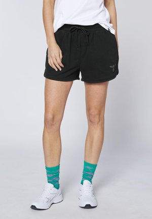 Person wearing black drawstring shorts, green patterned crew socks, white sneakers, and a white shirt against a plain background.