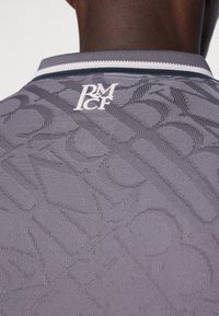 Camicia grigia a trama con un motivo discreto, colletto a coste con dettagli bianchi e un logo bianco sul retro vicino alla scollatura.