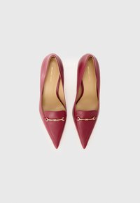 Décolleté in pelle bordeaux con punta affusolata e una catena dorata sopra il fronte. Texture liscia e design elegante, caratterizzato da una silhouette a bassa scollatura.