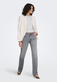 Blazer beige, t-shirt gris court et jean droit gris clair. Le mannequin porte des escarpins olive. Textures lisses et coupe ajustée.