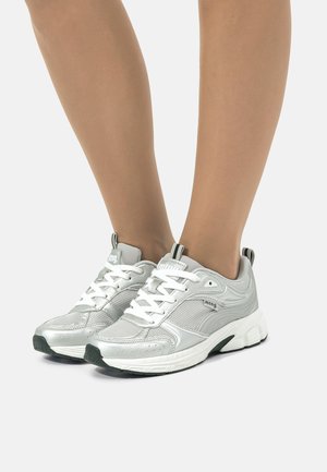 Zapatillas deportivas plateadas con material de malla y sintético, que presentan cordones blancos, acentos texturizados y suelas de goma negras.